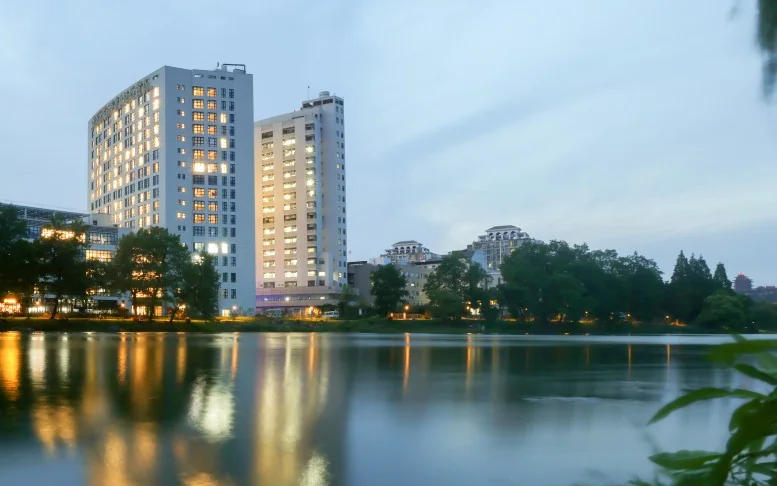 The Second Affiliated Hospital's inpatient towers at dusk, lit windows reflected in the water below.