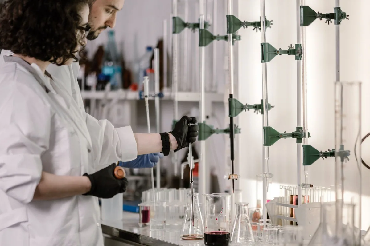 Two researchers working with titration glassware at a fume hood.