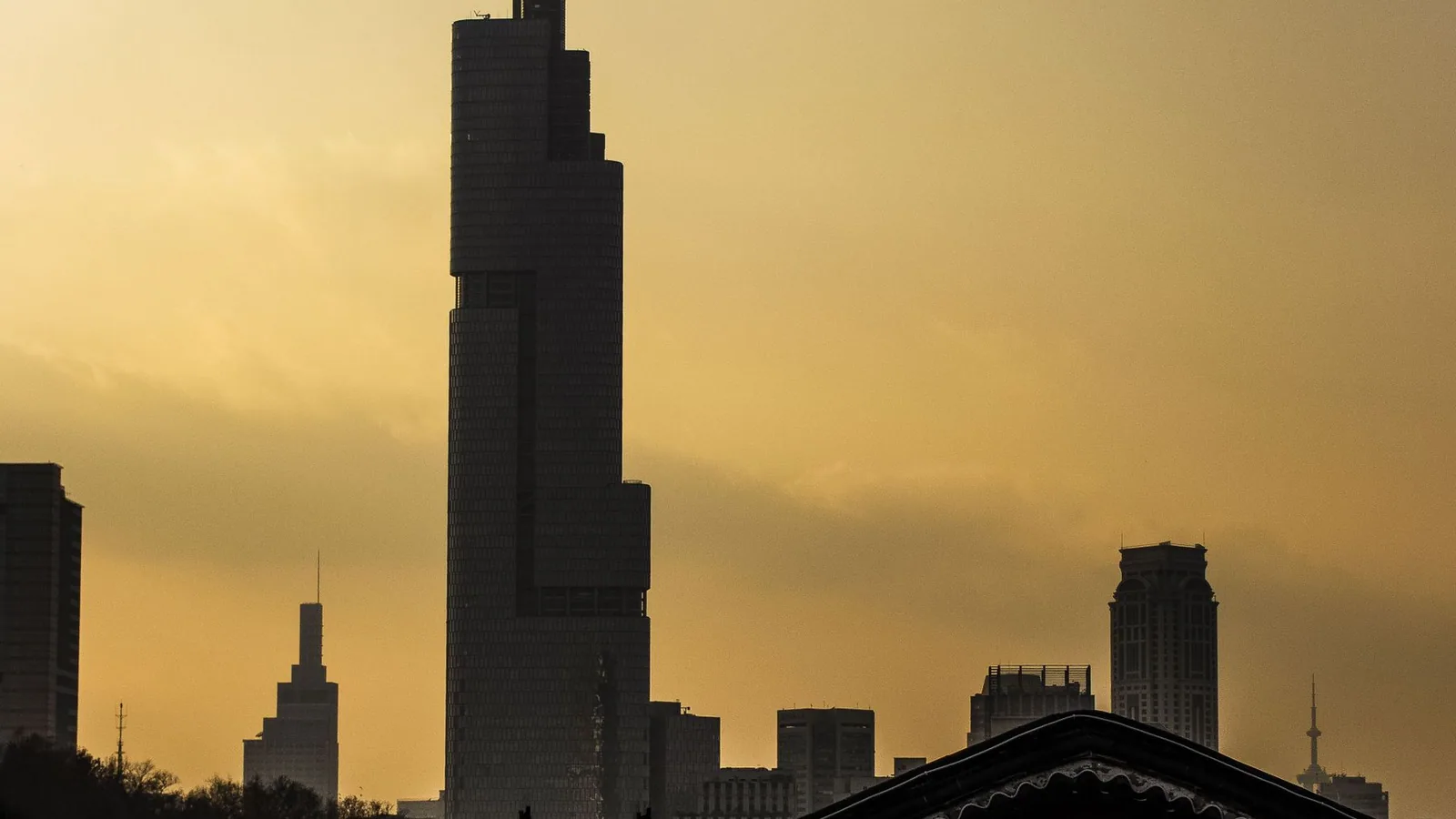 The Nanjing skyline at dusk, with a tower in silhouette above the old city wall.